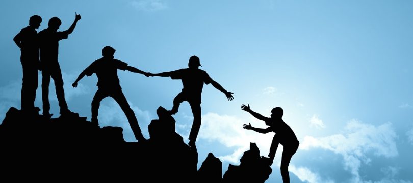 Silhouette of a group of people helping each other climb a mountain, arms outreached